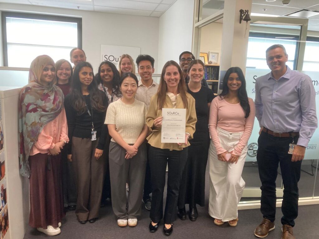 Mestranda da FCM-MG posa com pesquisadores durante mobilidade internacional na Austrália, exibindo certificado acadêmico